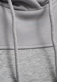 Felpa grigia chiaro con una finitura testurizzata, che presenta un logo prominente e lacci intrecciati per la regolazione. Materiale morbido in misto cotone.