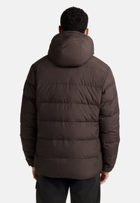 Giacca puffer marrone con cappuccio rotondo, design trapuntato e polsini elasticizzati. Caratterizzata da una texture liscia e da un taglio leggermente accorciato in vita.