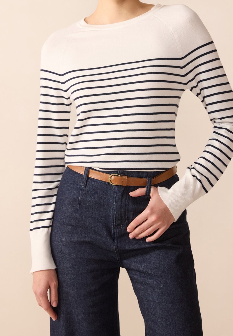 Personne portant un haut à manches longues blanc avec des rayures horizontales bleu marine, un jean taille haute bleu foncé, et une ceinture marron clair avec une boucle dorée.