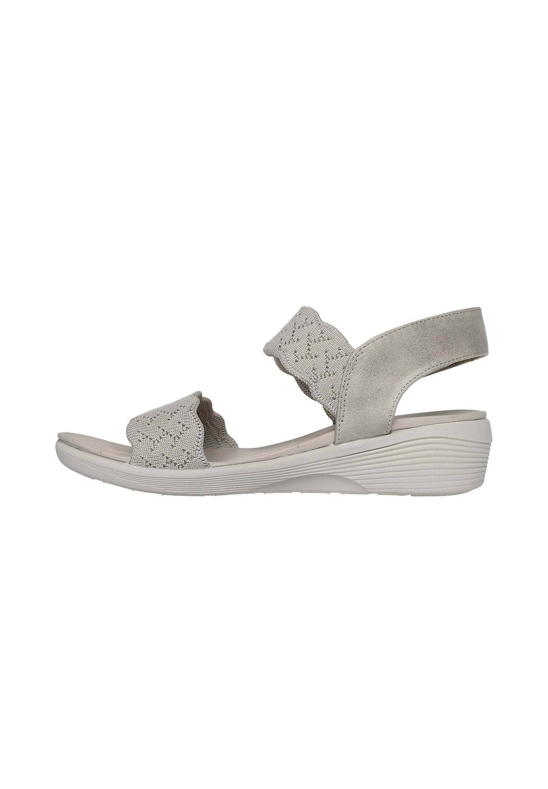 Sandalia de color gris claro con parte superior texturizada, acentos ondulados, correa ajustable y suela acolchada. Presenta un tacón cuña bajo y suela de goma.