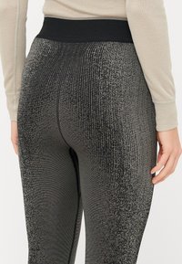 Høyt liv, svarte leggings med en teksturert metallisk glans, med ribbet mønster og en glatt elastisk midje.