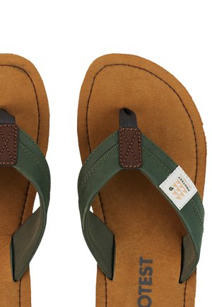 Bruine sloffen-sandalen met groene stoffen bandjes, bruin leren patch met stiksel en een wit label met de tekst "Protest" op één bandje.