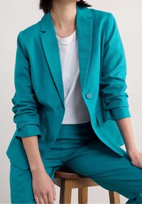 Miętowa marynarka na jedno guziki, dopasowanego kroju, z lekko podwiniętymi rękawami, zestawiona z białym t-shirtem i pasującymi miętowymi spodniami.