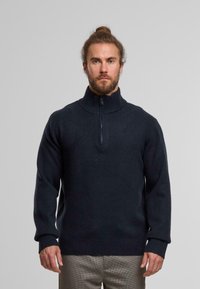 Navy zip-neck sweater with a high ribbed collar, knitted texture, and ribbed cuffs and hem. The design features a front zipper closure.