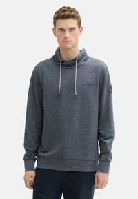 Grijze fleece pullover hoodie met een hoge hals, voorzien van een trekkoord, ribgebreide manchetten en een klein logo op de borst. Zachte textuur.