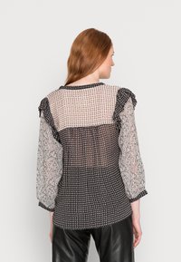 Blusa transparente com uma parte de trás preta e branca com padrão, yoke quadriculado e mangas com volantes; detalhes decorativos nas mangas.
