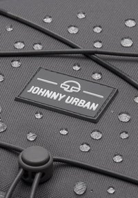 Black fabric backpack with a textured surface, featuring water droplets and a white logo patch. Includes a cinch closure with black cords.