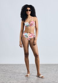 Krāsains ziedu bikini ar bezsiksnu augšdaļu un augsta vidukļa apakšdaļu. Ietver zilu, rozā un zaļu toņu maisījumu. Gluda auduma tekstūra.