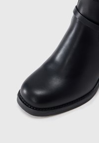 Μαύρο δερμάτινο μποτάκι μέχρι τον αστράγαλο με στρογγυλεμένη μύτη, λεία υφή και μινιμαλιστικό σχεδιασμό με αντίθετη λεπτομέρεια στη σόλα.