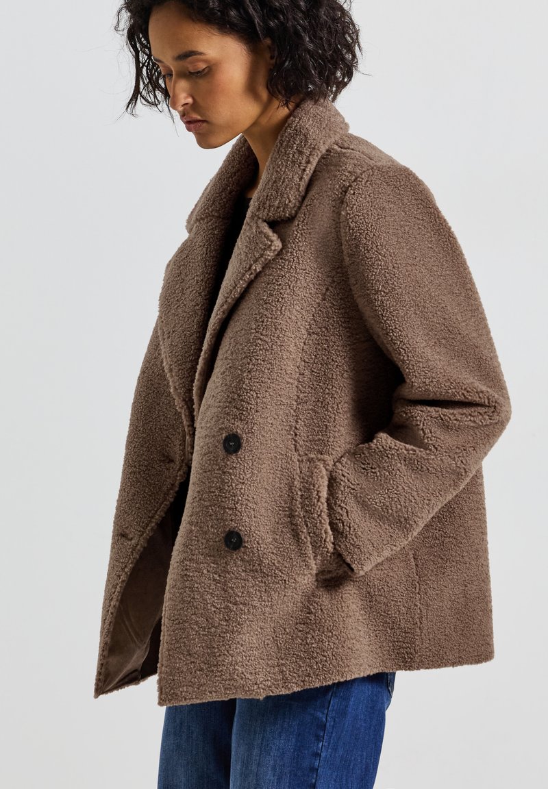 Veste en polaire marron avec une coupe décontractée, col à revers et deux boutons noirs. Comprend des poches latérales et une surface douce et texturée.