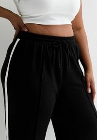 Zwarte joggers met witte zijsteken, gemaakt van zacht materiaal. Voorzien van een elastische tailleband met een trekkoord voor een aanpasbare pasvorm.