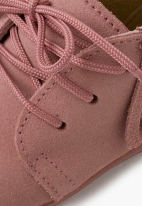Zapato de ante rosa con superficie texturizada, cordones a juego y costuras reforzadas a lo largo de los bordes. Vista en primer plano centrada en los detalles.