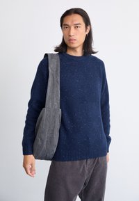Granatowy sweter dzianinowy z drobnym wzorem, okrągłym dekoltem i ściągaczami na końcach rękawów. Szara torba na ramię wykonana z miękkiego materiału.