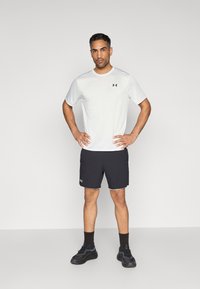 Ropa deportiva para hombre: camiseta blanca de manga corta, pantalones cortos negros con detalles en gris, zapatillas deportivas, diseño sólido con logo en la camiseta y los pantalones cortos.