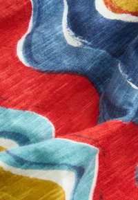 Tejido colorido con patrones audaces; presenta tonos rojos, azules, turquesas y amarillos; superficie suave y texturizada.