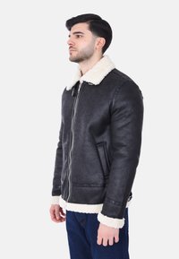Giubbotto in ecopelle nera con colletto e polsini in shearling bianco, dotato di zip frontale e tasche laterali, abbinato a jeans blu scuro.