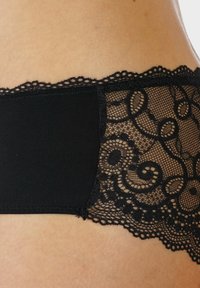 Mutande in pizzo nero con corpetto in tessuto nero liscio e dettagli in pizzo floreale intricati lungo la cintura, con bordi ondulati.