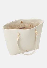 Vit handväska i konstläder med guldfärgade detaljer, slät textur och ett rymligt inre med en dragkedjeficka och logotyp.