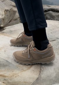 Beige Wanderstiefel aus Wildleder und Mesh mit grauen Akzenten und leuchtend orangefarbenen Ösen. Gore-Tex-Logo an der Seite sichtbar.