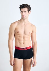 Schwarze Boxershorts mit rohem Bund, auf dem das "DIESEL"-Logo in Schwarz aufgedruckt ist. Glatter Stoff, figurbetontes Design, mittellange Beine.