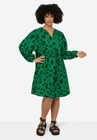 Groene jurk met een zwart luipaardprint, met een V-hals, ballonmouwen en een losse pasvorm. Draagt met zwarte sandaaltjes met straps.