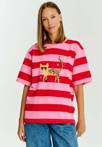 Červené a růžové pruhované tričko s potiskem žluté kočky s leopardím vzorem, která má sluneční brýle ve tvaru srdce a hvězdné akcenty. Krátké rukávy.