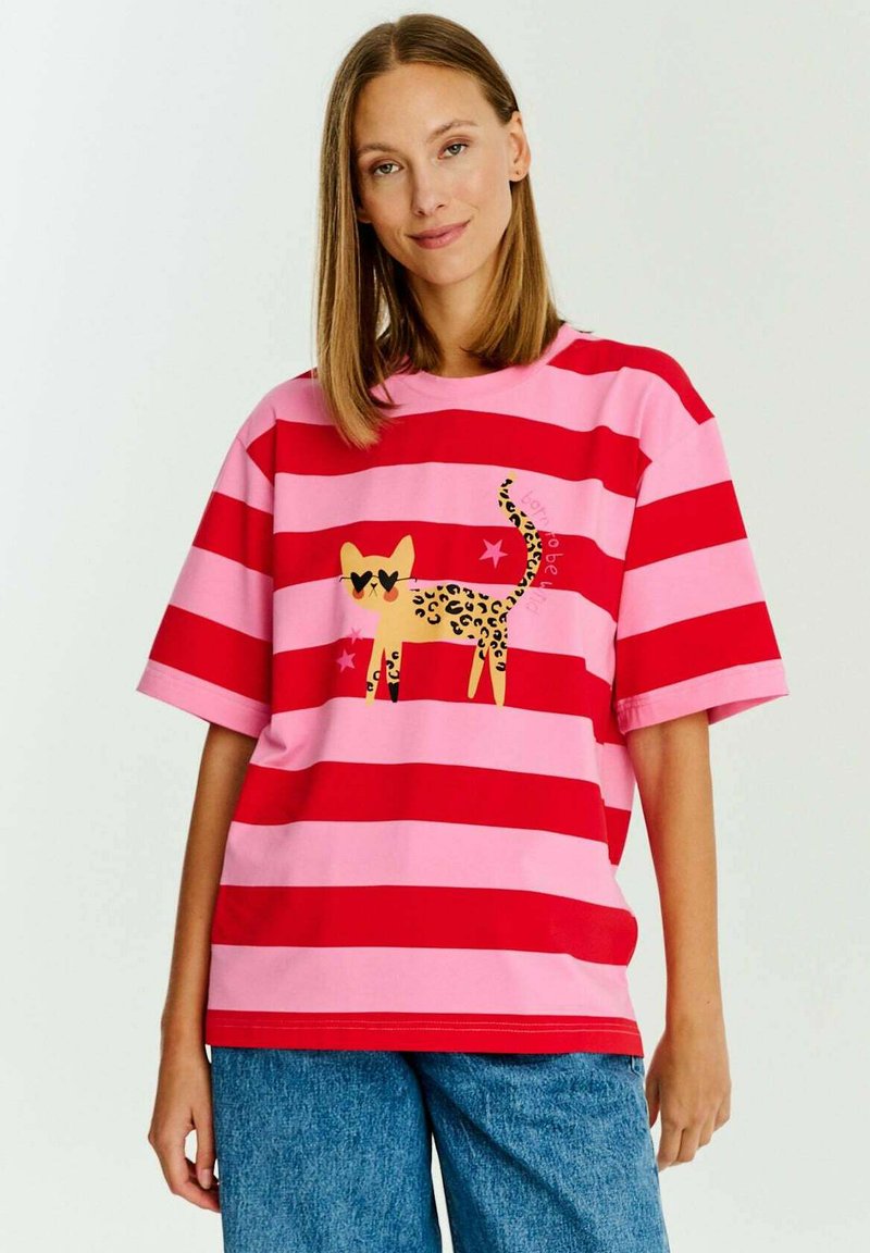 Červené a růžové pruhované tričko s potiskem žluté kočky s leopardím vzorem, která má sluneční brýle ve tvaru srdce a hvězdné akcenty. Krátké rukávy.