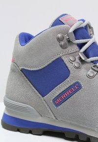 Botte de randonnée en daim gris et tissu bleu avec œillets métalliques, semelle grise et logo Merrell. Design à lacets avec col rembourré.