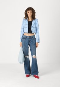 Lyseblå cropped jakke med rutemønster, svart tettsittende topp, blå jeans med hull, røde sko, og en lys blå veske.