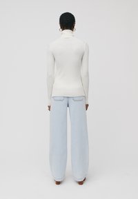 Pull à col roulé blanc côtelé au design ajusté, associé à un jean large bleu clair. Présente une texture douce et une coupe longueur cheville.