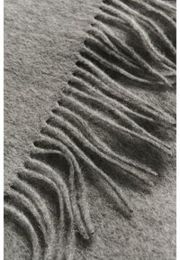 Blød grå uldstof med jævnt fordelte, lange frynser langs den ene kant i nærbillede.