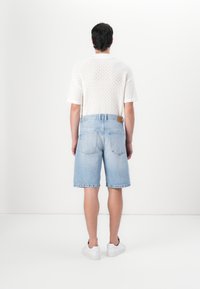 Camisa blanca de punto de manga corta, pantalones cortos de mezclilla azul claro de corte relajado y zapatillas blancas. Diseño simple sin patrones visibles.