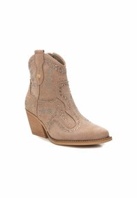 Botín de ante color marrón claro con punta afilada y tacón apilado. Decorado con tachuelas plateadas en patrones de estrellas y detalles de costura en contraste.