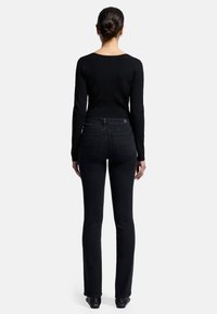 Schwarzer, enganliegender Pullover mit langen Ärmeln und Rundhalsausschnitt, kombiniert mit dunklen Bootcut-Jeans, die ein dezentes Design der Gesäßtaschen aufweisen.