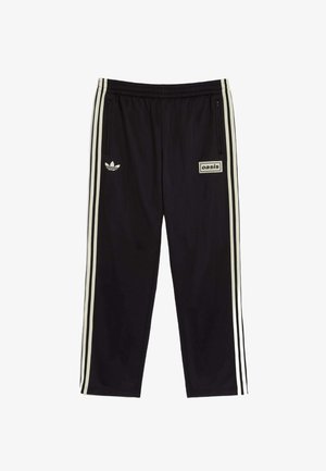 Czarne spodnie sportowe wykonane z gładkiego materiału, z białymi akcentami w postaci trzech pasków, haftowanym logo oraz prostokątną naszywką z napisem 'oasis'.