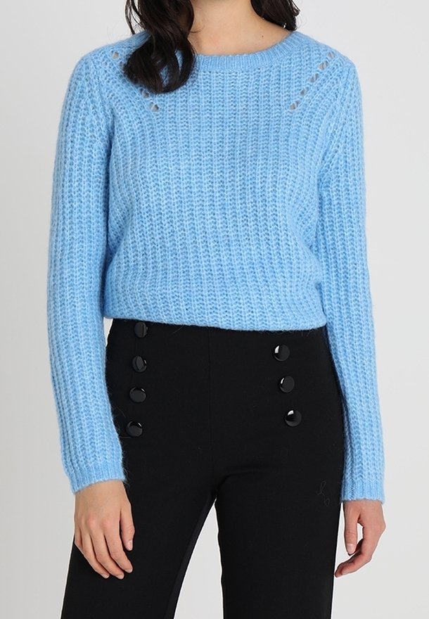 Ljusblå stickad tröja med ett strukturerat mönster, rundad halsringning och små utskärningar vid axlarna, kombinerad med svarta byxor med knappar.