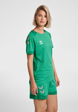Grøn sportsjersey og shorts sæt, lavet af åndbart mesh-stof. Har grå chevron-detaljer på skuldrene og shortsene.