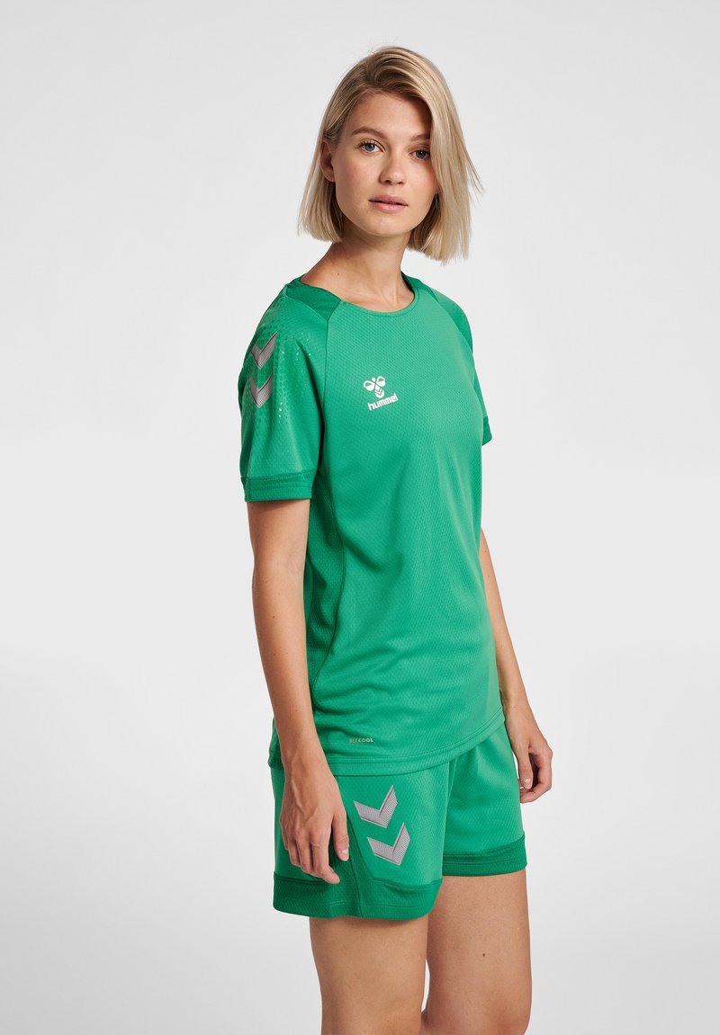 Grön sporttröja och shorts-set, tillverkat av andningsbart meshmaterial. Har grå chevrondetaljer på axlarna och shortsen.