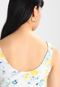 Débardeur floral avec un fond blanc, orné de fleurs jaunes, bleues et roses. Tissu doux ; larges bretelles et un dos en forme de scoop.