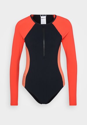 Hosszú ujjú neopréna ruha, tengerészkék alapszínen korallszínű díszítéssel, elöl cipzárral, és a "ROXY" logóval az oldalon. Rugalmas anyagból készült.