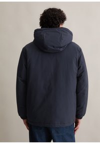 Granatowa pikowana kurtka z dużym, regulowanym kapturem, elastycznymi mankietami oraz gładką, matową teksturą. Posiada luźny krój.