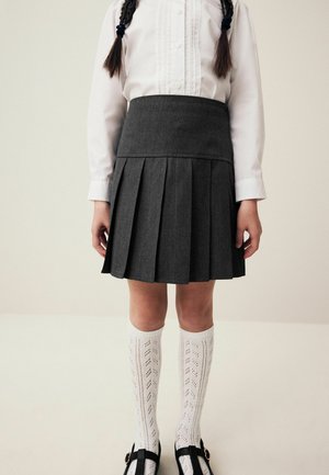 Gonna grigia a pieghe realizzata in un tessuto con finitura testurizzata, abbinata a calze bianche fino al ginocchio con un design a motivi e scarpe nere.