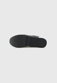 Black sneaker sole with ridges and a slightly rounded tip. Material appears rubber with a textured finish for traction.
