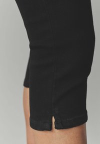 Pantalones capri de mezclilla negra con un diseño ajustado; cuentan con un detalle de corte en el dobladillo y un acabado de tejido texturizado.
