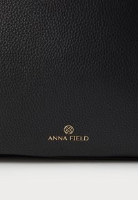 Must mustriga nahast kott, millel on alumises nurgas kuldne "ANNA FIELD" logo. Lihtne disain minimaalsete aksessuaaridega.