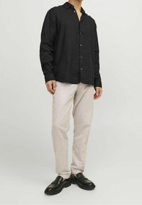 Camicia nera di lino a maniche lunghe con bottoni, abbinata a pantaloni di lino beige chiaro e mocassini neri con suola spessa.