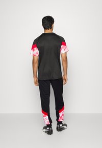 Träningskläder bestående av en svart kortärmad topp med röda och rosa tie-dye detaljer, tillsammans med svarta byxor med röda och rosa sidodetaljer.