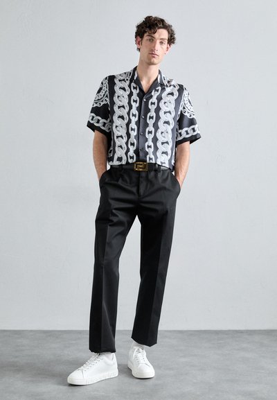Camisa de manga corta de seda negra con patrón de cadenas blancas, combinada con pantalones negros y zapatillas blancas con una suela texturizada.