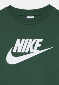 Zelena bombažna kapuca z velikim belim Nike logotipom in znakem. Tkanina je gladka z rebrastim izrezi pri vratu.