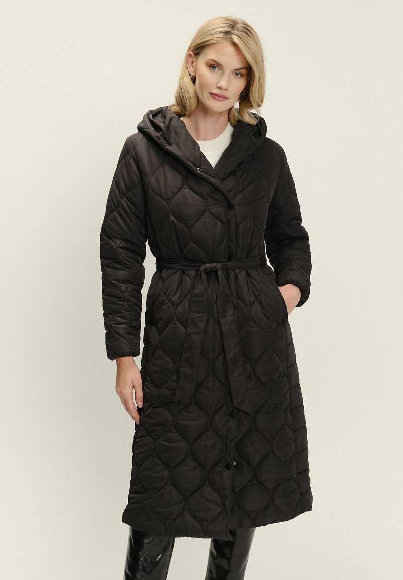 Čierny prešívaný dlhý kabát s kapucňou, obsahujúci opasok v páse a zapínanie na gombíky, vyrobený z hladkej, lesklej látky s jemnou textúrou.